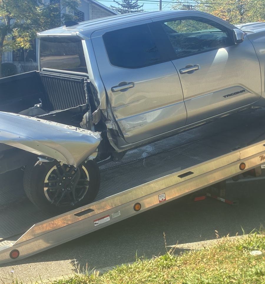 A silver Toyota Tacoma with heavy rear damage being winched up the tilted bed of a tow truck.