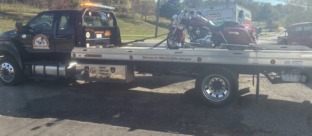 Butler's black flatbed with a red Harley-Davidson strapped to the bed in a parking lot.
